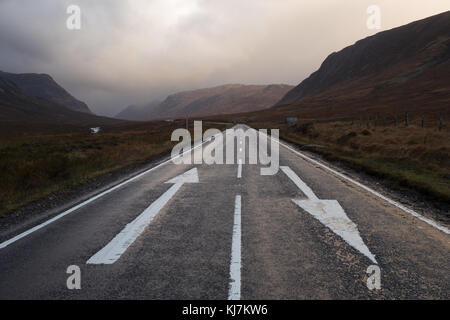 A82 durch Glencoe, Schottland, UK mit Richtungspfeile in der Straße im Winter in der Dämmerung Stockfoto