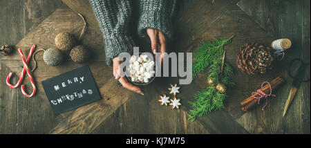 Weihnachten, Neujahr Vorbereitung Hintergrund. Grusskarte, glitzerndes Spielzeug, Frauenhände in grauem Pullover mit Becher heißer Schokolade, cin Stockfoto