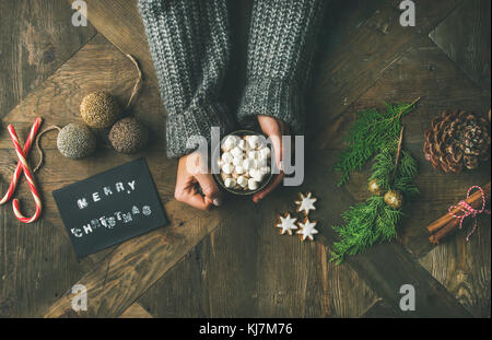 Weihnachten, Neujahr Hintergrund. Grusskarte, glitzerndes Spielzeug, Frauenhände in grauem Strickpullover mit Becher heißer Schokolade, Zimt Stockfoto