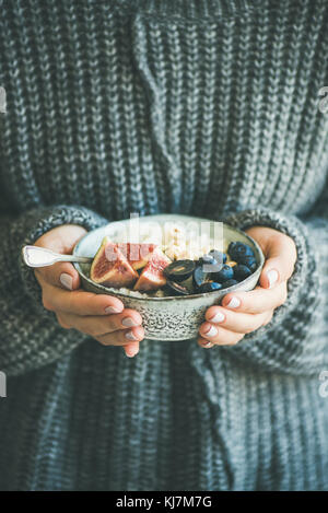 Gesund im Winter Frühstück. Frau in Wollpullover holding Schüssel Reis Kokosnuss Porridge mit Feigen, Beeren, Haselnüssen. Sauber Essen, vegetarische, vegane Stockfoto