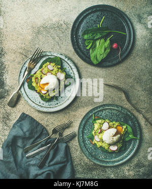 Gesunde vegetarische Frühstück Flachbild-legen. Vollkorn Toast mit Avocado, Spinat, Rettich und pochiertem Ei auf Platten über grauer Beton Hintergrund, oben vi. Stockfoto