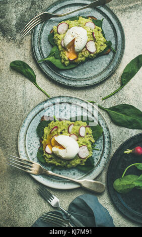 Gesunde vegetarische Frühstück Flachbild-legen. Whole-grain Toasts mit Avocado, Spinat und pochierte Eier über grauer Beton Hintergrund, Ansicht von oben. Sauber, Essen Stockfoto