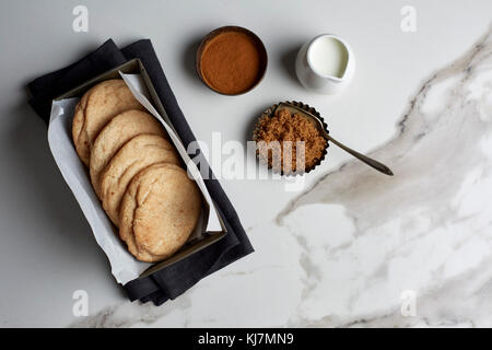 Snickerdoodle cookies mit Zutaten in vintage Dosen auf weißem Marmortisch mit schwarzem Leinen Stockfoto