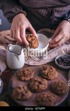 Frau essen Kürbis Chocolate Chip Cookies mit einer Tasse Milch Stockfoto