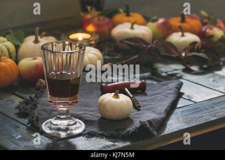 Herbsturlaub Tischdekoration mit dekorativen Kürbissen, Äpfeln, roten Blättern, Gläsern Rotwein, Kerze über Holztisch. Rustikaler Stil, Tag Stockfoto