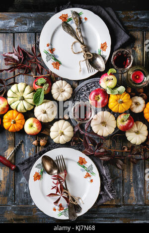 Herbstferien Tischdekoration mit dekorative Kürbisse, Äpfel, rote Blätter, leerer Teller mit Besteck, Rotwein, Kerze über Holz- t Stockfoto