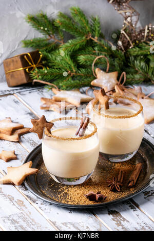 Eierwein Weihnachts-Milchcocktail mit Zimt, serviert in zwei Gläsern auf Vintage-Tablett mit Shortbread Stern Form Zucker Kekse, Dekor-Spielzeug, Tannenzweig o Stockfoto