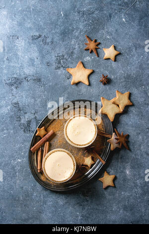 Eierwein Weihnachtsmilch Cocktail mit Zimt, serviert in zwei Gläsern auf vintage Tablett mit Shortbread Stern Form Zucker Cookies unterschiedlicher Größe über blau Stockfoto