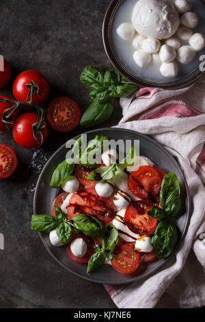 Italienische Caprese Salat mit in Scheiben geschnittenen Tomaten, Mozzarella, Basilikum, Olivenöl. In vintage Metallplatte mit Zutaten oben über Dark Metal serviert. Stockfoto