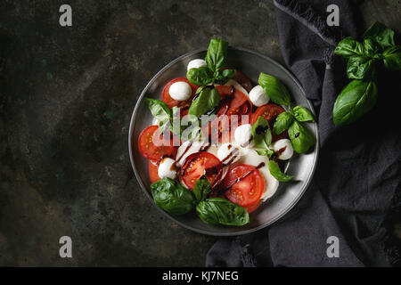 Italienische Caprese Salat mit in Scheiben geschnittenen Tomaten, Mozzarella, Basilikum, Olivenöl. In vintage Metallplatte auf textile Serviette über Dark Metal Hinterg serviert. Stockfoto