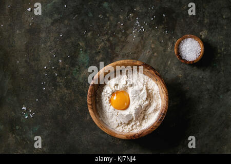 Olivenholz Schüsseln mit Meersalz, Weizenmehl und ganze Eigelb über Altes, dunkles Metall Hintergrund. Ansicht von oben mit der Kopie. Backen Konzept Stockfoto