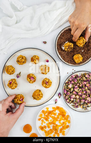 Ein Mann und eine Frau, die Kürbis Kugeln von der Ansicht von oben fotografiert. Die gewürfelten Aprikosen, Leinsamen und Rosenblättern begleiten. Stockfoto