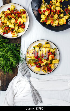 Vegane Kartoffel Salat mit gegrillten Paprikas in einem schwarzen Schüssel und auf zwei kleinere weiße Platten von der Ansicht von oben fotografiert. Frischer Dill und Knoblauch auf einer Stockfoto