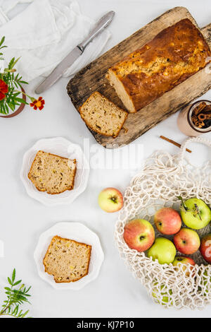 Cinnamon Apple Brot in Scheiben geschnitten auf einer hölzernen Schneidebrett aus Sicht von oben fotografiert. Äpfel in einem Netzbeutel und Apple Brotscheiben auf beiden Platten begleiten. Stockfoto