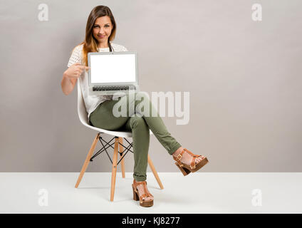 Schöne Frau sitzt auf einem Stuhl und etwas zeigt auf einem Laptop Stockfoto