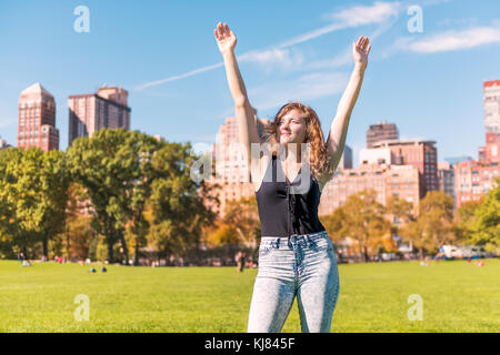 Nahaufnahme der eine glückliche junge Frau mit ausgestreckten Händen, die Arme in der Luft im Central Park in New York City New York City während der sonnigen Herbsttag mit modernen Stockfoto