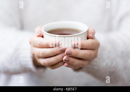 Lifestyle Foto von der Nähe zu einer jungen Frau mit einer Tasse Kräutertee in einem weißen Becher Tragen eines weißen wollenen Pullover. Stockfoto