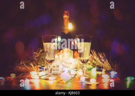 Gläser mit Champagner stehen auf einem Holztisch vor dem Hintergrund der Lichter von einer Girlande. zwei Gläser Champagner Schiebeschalter gegen bokeh Leuchten b Stockfoto