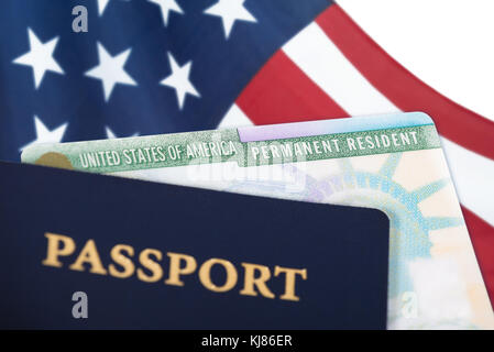 Vereinigte Staaten von Amerika Permanent Resident Card, Green Card, mit der amerikanischen Flagge im Hintergrund und einem Pass im Vordergrund angezeigt. Die Einwanderung Stockfoto