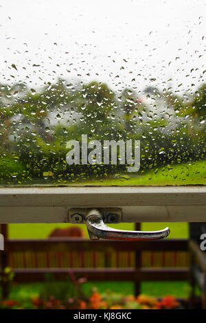 Regentropfen auf Fenster mit Garten im Hintergrund Stockfoto