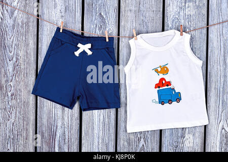 Baby Kleidung hängend am Seil. Infant Boy Shorts und T-Shirt trocknen auf der Wäscheleine auf alten Holz- Hintergrund. Stockfoto