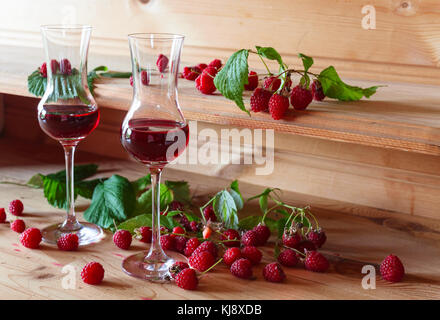 Hausgemachte himbeere Wein und reife Beeren mit Blätter auf einen hölzernen Tisch. Stockfoto