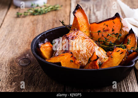 Hausgemachte gebratenes Hähnchen Schenkel mit Kürbis und Thymian Kraut in Gusseisen Skillet auf ländlichen Holztisch Stockfoto