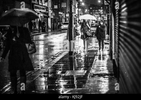 Abendlicher Blick auf der Suche nach Thomas Street, Central Manchester. Frauen werden durch ein Schaufenster beleuchtet, wie sie ihren Weg durch die Rush-hour Regen Stockfoto