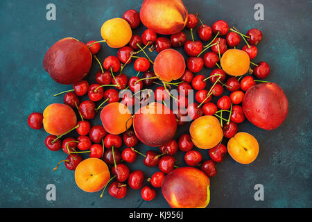 Zusammensetzung reif organische Sommer Früchte Beeren süsse Kirschen Nektarinen Aprikosen lebendige Farben auf dunkelblauem Hintergrund. Ernte sauber essen gesund Stockfoto