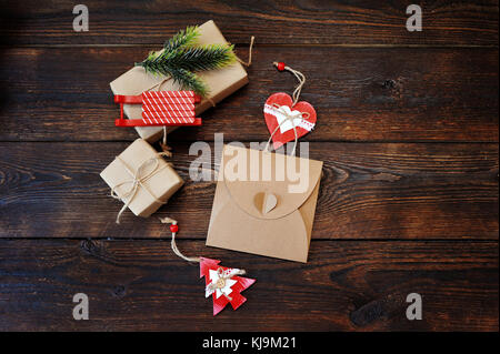 Weihnachten Zusammensetzung der Geschenk Kraftpapier Boxen mit einem Dekor aus Tanne, Schlitten und Herzen auf hölzernen Hintergrund. Flach, Ansicht von oben Foto mockup Stockfoto