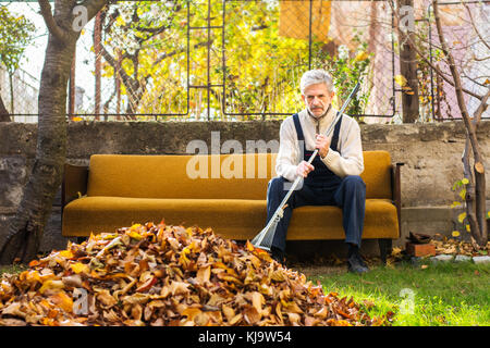 Müde älterer Mann Rest von Reinigung gefallenen Blätter im Herbst im Hof Stockfoto