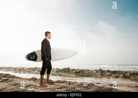 Der Unternehmer hält ist Surfbrett nach einem langen Tag der Arbeit Stockfoto