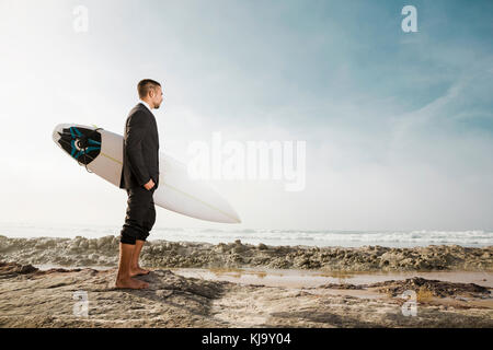 Der Unternehmer hält ist Surfbrett nach einem langen Tag der Arbeit Stockfoto