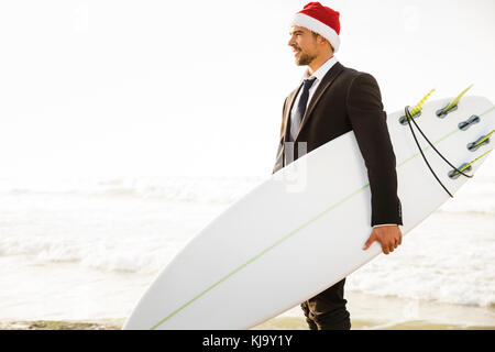 Business surfer Tragen eines Santa Hut und halten ein Surfbrett Stockfoto