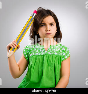 Studio Portrait von einem kleinen Mädchen denken und den Kopf kratzen mit einem großen Bleistift Stockfoto