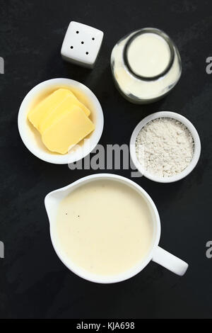 Hausgemachte französische Béchamelsoße oder weiße Soße serviert in Sauce Boot mit Zutaten auf der Seite (Mehl, Butter, Milch), Overhead auf schiefer fotografiert. Stockfoto