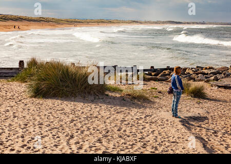 Eine Frau am Strand von Seaton Sluice steht in der Landschaft suchen, die Nordsee Wellen brechen am Strand zu sprühen und Haze, Northumberland, Großbritannien Stockfoto