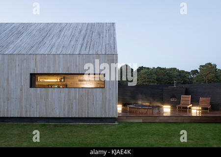 Ansicht der Fassade in der Dämmerung mit Whirlpool. Watson House Anhang, Brockenhurst, Vereinigtes Königreich. Architekt: Strom Architekten, 2017. Stockfoto