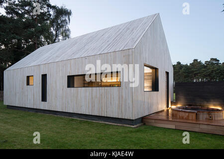 Ansicht der Vorder- und der Osten Fassade in der Dämmerung mit Whirlpool. Watson House Anhang, Brockenhurst, Vereinigtes Königreich. Architekt: Strom Architekten, 2017. Stockfoto