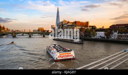 Anzeigen von Millennium Fußgängerbrücke in Richtung der Shard und Tower Bridge mit City Cruises Yacht Passing auf der Themse. Mit Tilt Shift Effekt. Stockfoto