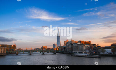 Ein Blick auf die Southwark Bridge und The Shard in London wie die Sonnenuntergänge und einen goldenen Glanz der Gebäude als Flugzeug Overhead. Stockfoto