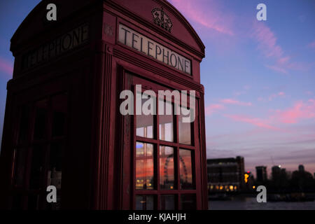 Traditionelle englische Telefon Red Box in London mit Sonnenuntergang in Windows wider. Stockfoto