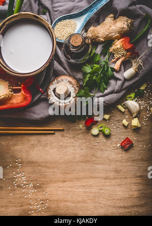 Vegetarische asiatische Küche Zutaten mit gehacktem Gemüse, Kokosmilch, Samen, Gewürze und Essstäbchen auf rustikalen Holzmöbeln Hintergrund, Ansicht von oben. Stockfoto