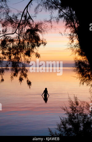 Eine einsame Frau Badegast wird reflektiert, wie sie den ruhigen Wasser der Ägäis. Sie ist gegen die flammenden Farben einer Dämmerung Himmel. Stockfoto