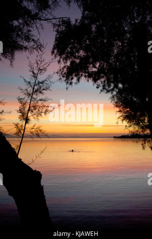 Das ruhige Meer spiegelt das helle orange Dämmerung Himmel und plätschert der fernen, silhouetted Kopf eines einsamen Schwimmer umgeben. Stockfoto