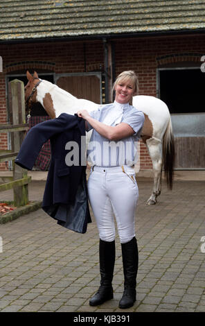 Elegant gekleideter Reiter, der eine dunkelblaue Reitjacke aufsetzt, November 2017 Stockfoto