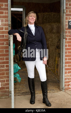 Elegant gekleideter Reiter, der in dunkelblauer Reitjacke, Jodphurs und Stiefeln an einer stabilen Tür steht. November 2017 Stockfoto