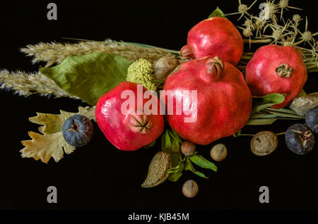 Granatapfel Obst mit Mandeln, Nüssen und Beeren, trockene Blätter und Zweige auf schwarzem Holz Hintergrund Stockfoto