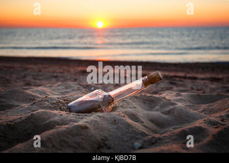 Nachricht mit dem Buchstaben in der Flasche am Strand im Sonnenuntergang Stockfoto