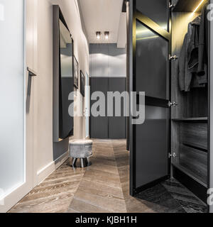 Eleganter Hausflur mit schwarzem Kleiderschrank, Holzboden und großem Spiegel Stockfoto